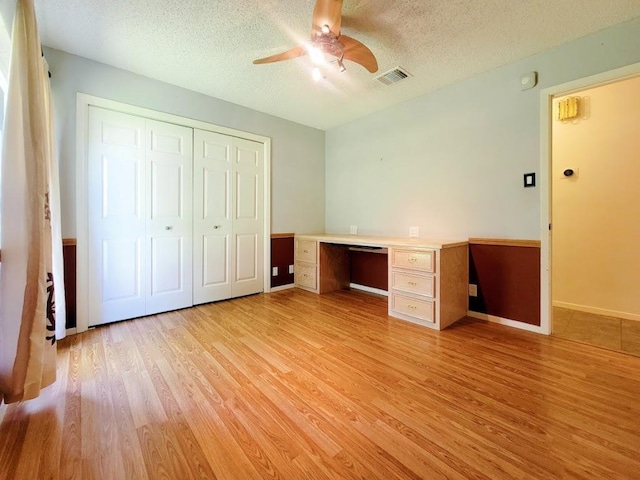 unfurnished office with visible vents, light wood-style flooring, a ceiling fan, a textured ceiling, and baseboards