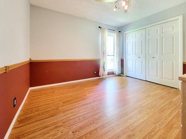 unfurnished bedroom featuring a closet, a textured ceiling, baseboards, and wood finished floors