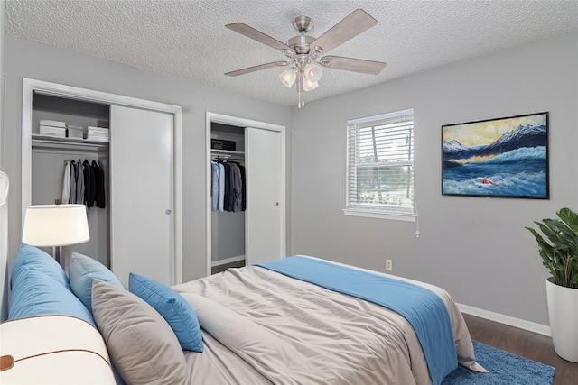 bedroom with baseboards, a ceiling fan, wood finished floors, a textured ceiling, and two closets