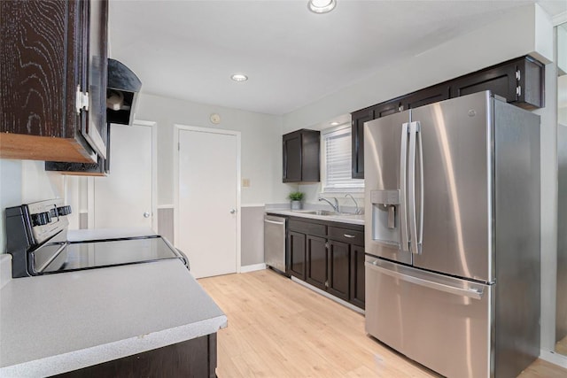 kitchen with a sink, light countertops, appliances with stainless steel finishes, dark brown cabinets, and light wood-type flooring