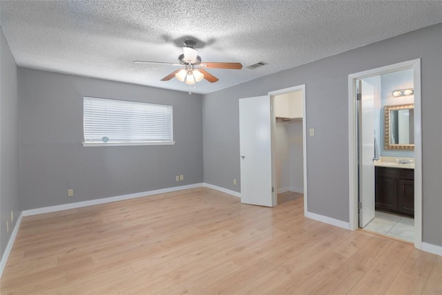 unfurnished bedroom featuring a walk in closet, a closet, visible vents, light wood-style flooring, and baseboards