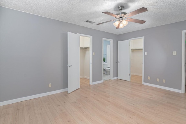 unfurnished bedroom with a closet, light wood-type flooring, a walk in closet, and visible vents