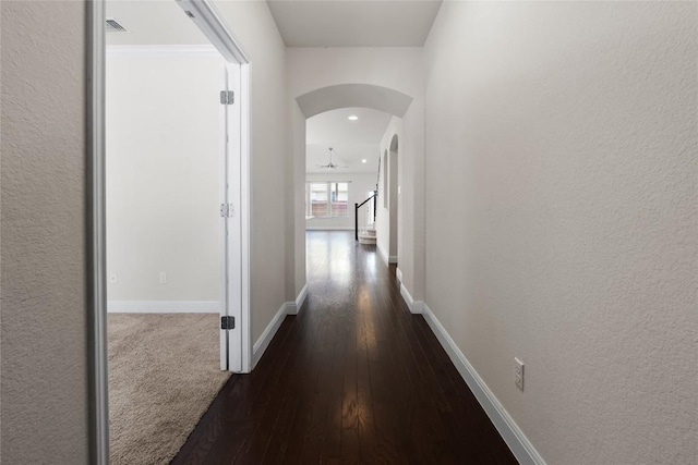 corridor with arched walkways, dark wood finished floors, visible vents, and baseboards