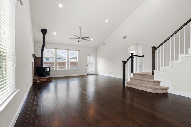 unfurnished living room with high vaulted ceiling, wood finished floors, visible vents, stairway, and a wood stove