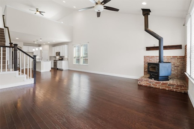 unfurnished living room featuring a wood stove, dark wood-style floors, stairs, and a ceiling fan