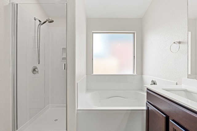 full bath featuring a stall shower, a textured wall, vanity, and a bath