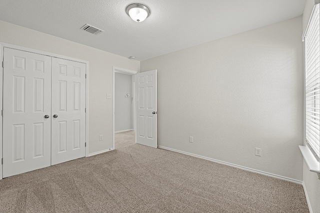 unfurnished bedroom featuring a textured ceiling, carpet floors, visible vents, baseboards, and a closet