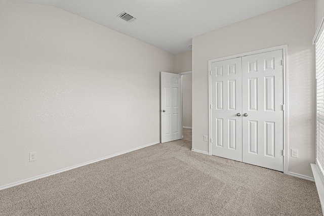 unfurnished bedroom with carpet flooring, visible vents, baseboards, vaulted ceiling, and a closet