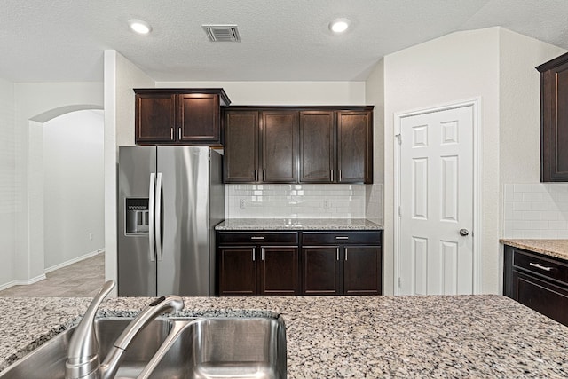 kitchen featuring visible vents, decorative backsplash, a sink, dark brown cabinetry, and stainless steel fridge