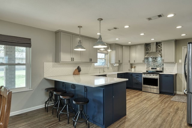 kitchen featuring wall chimney range hood, visible vents, stainless steel appliances, and gray cabinetry