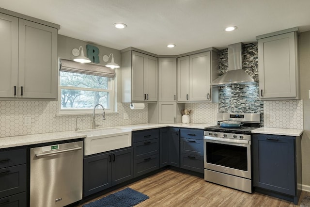 kitchen featuring stainless steel appliances, gray cabinetry, light wood-style floors, a sink, and wall chimney range hood