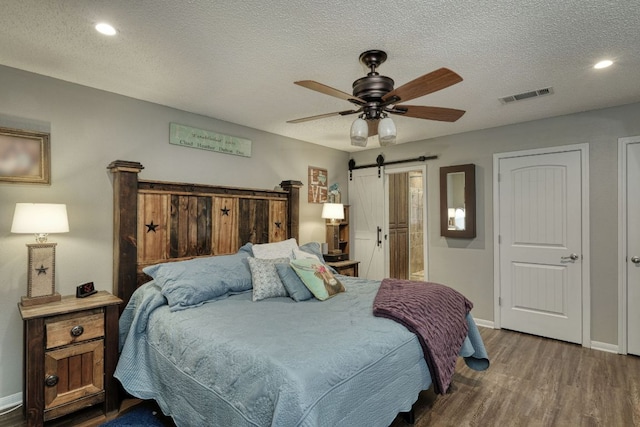 bedroom with visible vents, a barn door, a textured ceiling, wood finished floors, and baseboards