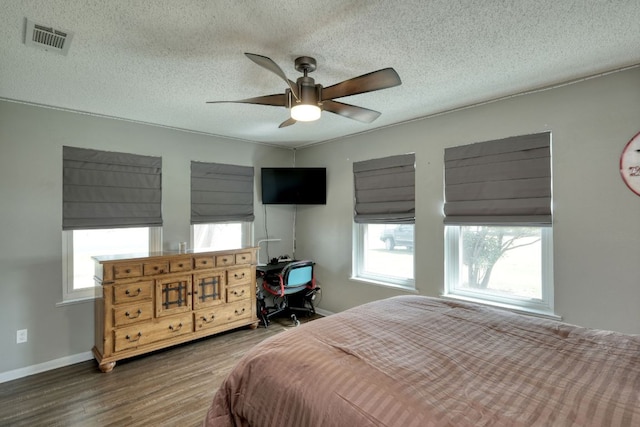 bedroom featuring baseboards, a textured ceiling, visible vents, and wood finished floors