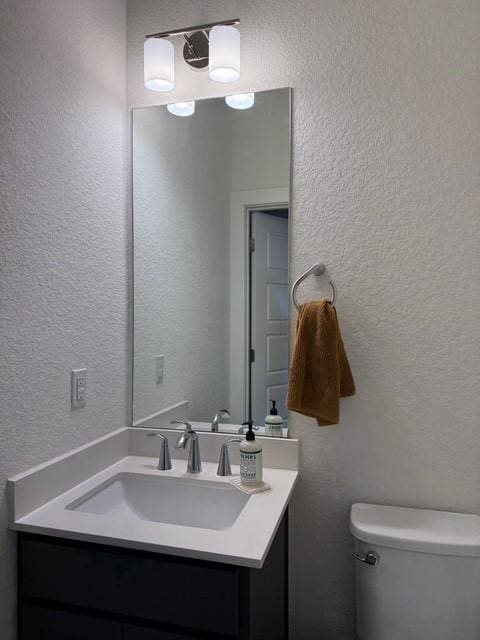 bathroom with a textured wall, vanity, and toilet