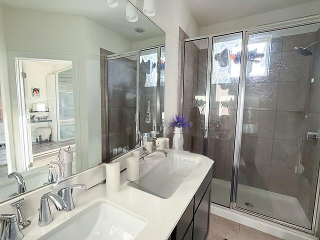 full bath featuring tile patterned flooring, a sink, a shower stall, and double vanity