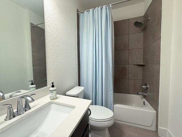 bathroom featuring a textured wall, tile patterned flooring, toilet, vanity, and shower / bath combination with curtain