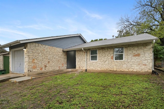 rear view of property featuring stone siding, a lawn, and an attached garage