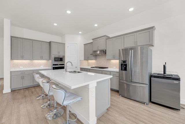 kitchen with under cabinet range hood, a sink, appliances with stainless steel finishes, light wood-type flooring, and gray cabinets