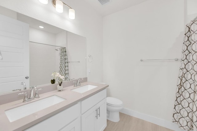 bathroom featuring double vanity, a sink, toilet, and baseboards