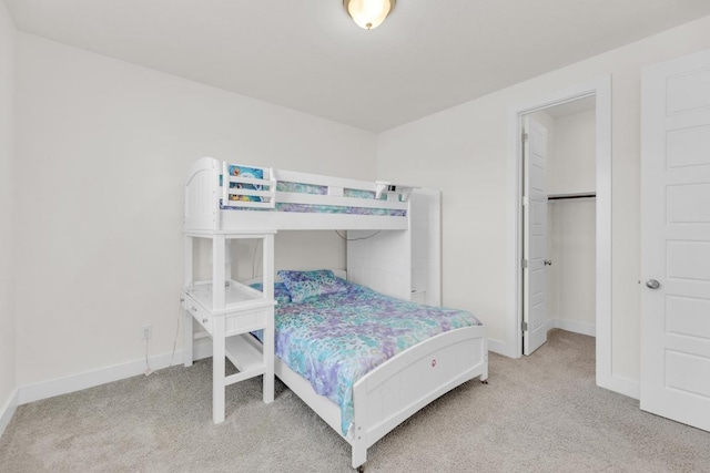 bedroom with a walk in closet, light colored carpet, and baseboards