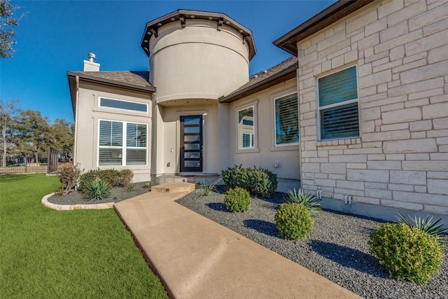 entrance to property featuring roof with shingles, a chimney, stucco siding, stone siding, and a lawn