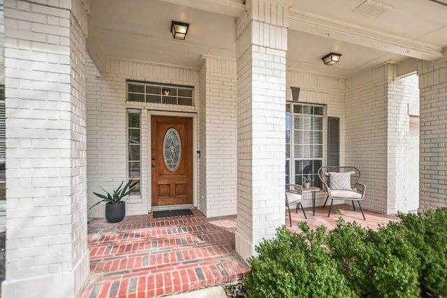 doorway to property featuring a porch and brick siding