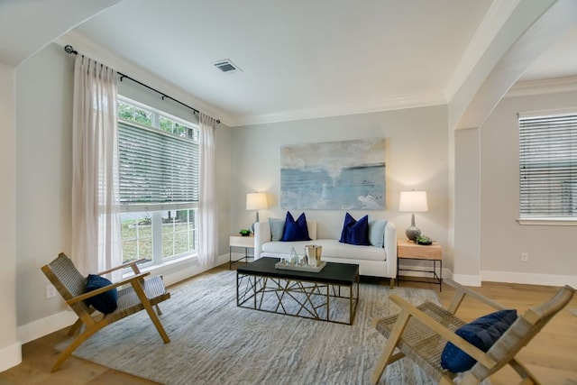 living area featuring baseboards, visible vents, crown molding, and wood finished floors