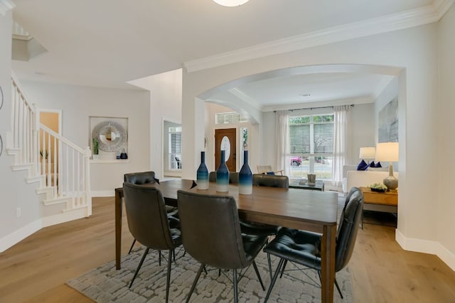 dining area with arched walkways, crown molding, stairway, light wood-type flooring, and baseboards