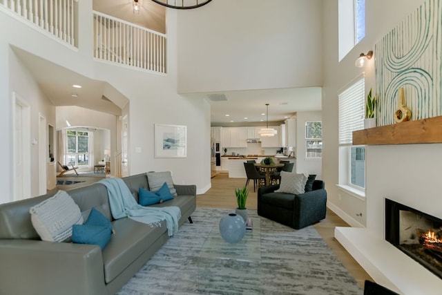 living area featuring arched walkways, light wood finished floors, visible vents, a lit fireplace, and baseboards