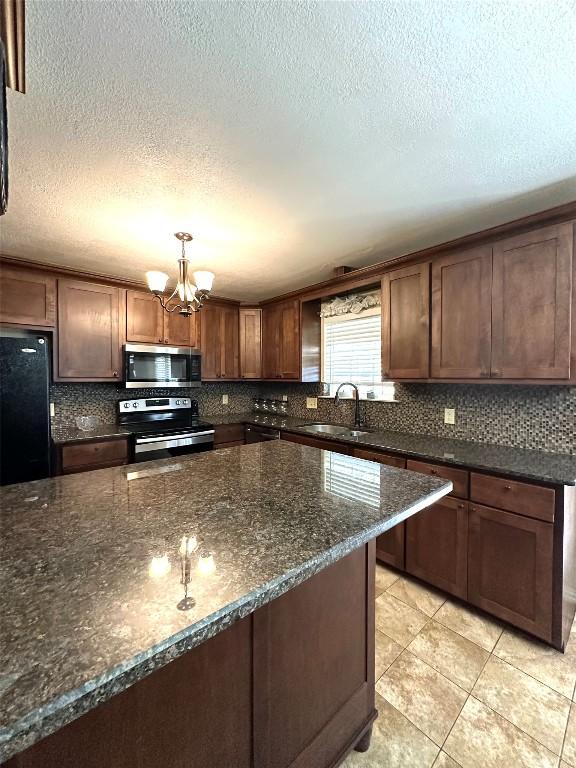 kitchen featuring a notable chandelier, tasteful backsplash, appliances with stainless steel finishes, a sink, and dark stone countertops