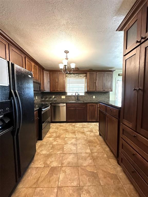 kitchen featuring appliances with stainless steel finishes, dark countertops, a sink, and a notable chandelier