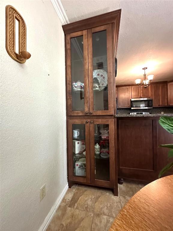 interior space with baseboards, a textured wall, stainless steel microwave, an inviting chandelier, and a textured ceiling