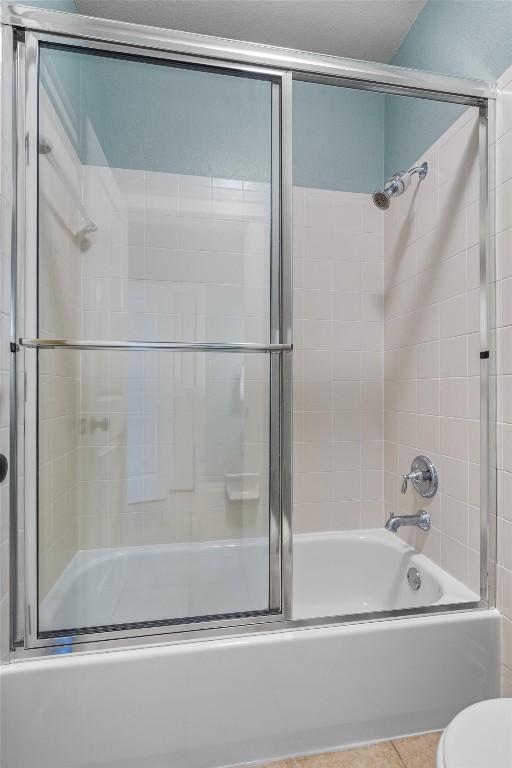 bathroom with toilet, tile patterned flooring, and combined bath / shower with glass door