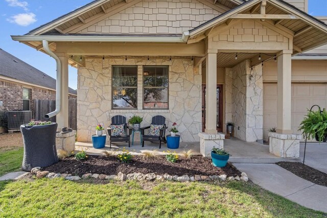 property entrance featuring stone siding, central AC unit, a garage, covered porch, and fence