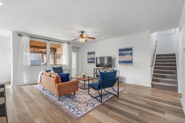 living room with stairs, wood finished floors, ceiling fan, and baseboards