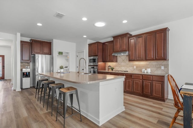kitchen featuring stainless steel appliances, under cabinet range hood, a sink, a breakfast bar area, and light wood-style floors