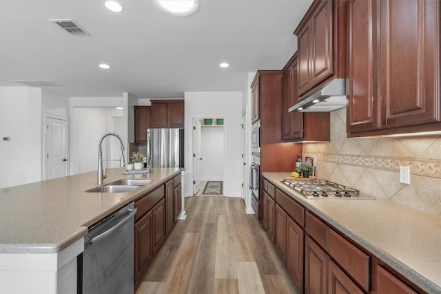 kitchen with stainless steel appliances, visible vents, a sink, light wood-type flooring, and under cabinet range hood