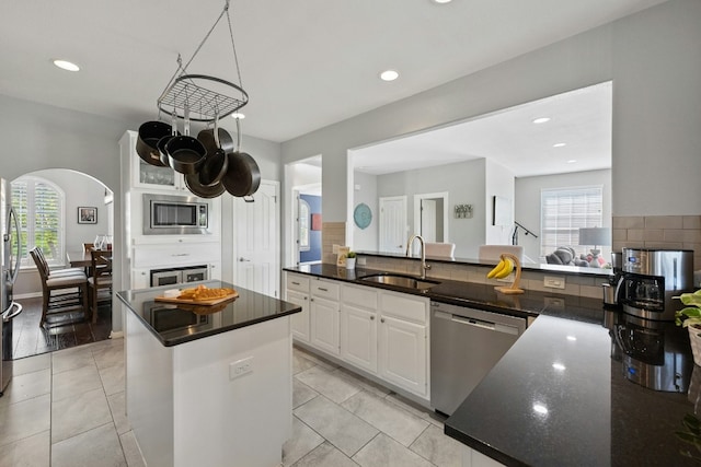 kitchen with light tile patterned floors, a kitchen island, stainless steel appliances, white cabinetry, and a sink