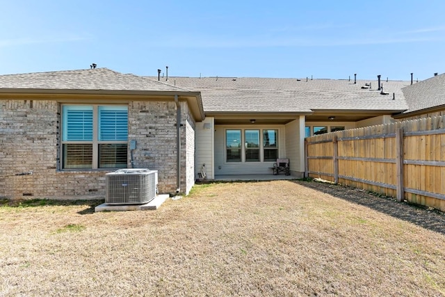 back of house featuring central air condition unit, fence, a lawn, and roof with shingles