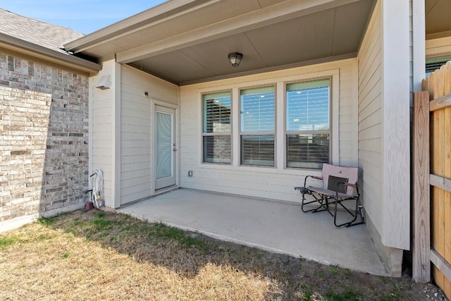 view of exterior entry featuring a patio, fence, brick siding, and roof with shingles