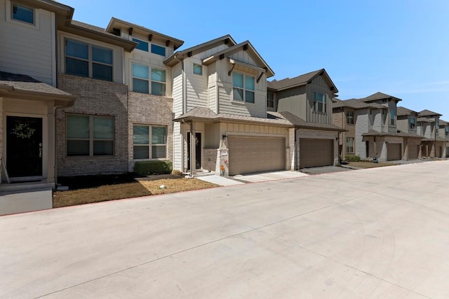 view of property featuring driveway, brick siding, a garage, board and batten siding, and a residential view