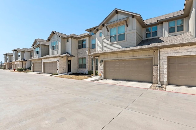 townhome / multi-family property with a residential view, board and batten siding, an attached garage, and stone siding