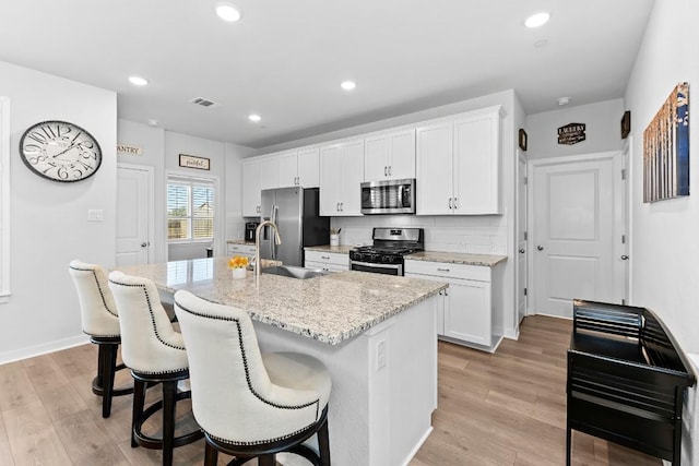 kitchen with visible vents, a kitchen island with sink, a sink, appliances with stainless steel finishes, and light wood finished floors