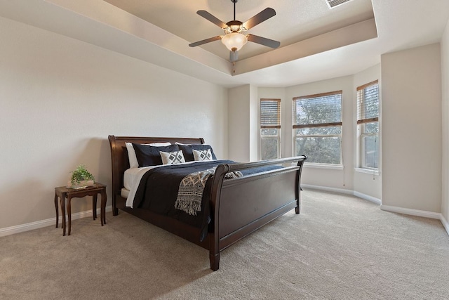 bedroom featuring ceiling fan, light carpet, visible vents, baseboards, and a tray ceiling