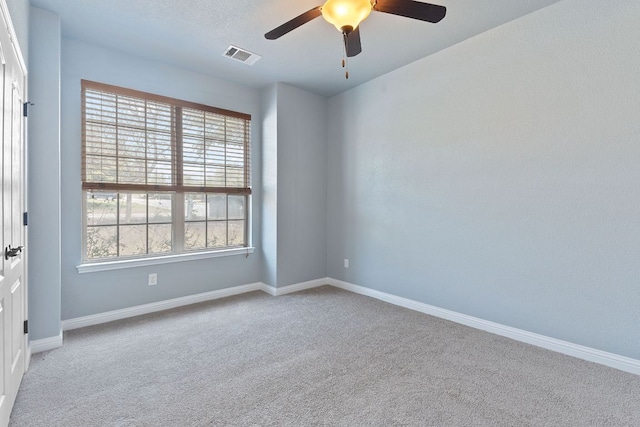 carpeted empty room featuring a ceiling fan, visible vents, and baseboards