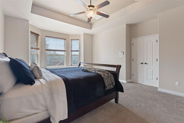 carpeted bedroom featuring a raised ceiling, a ceiling fan, and baseboards