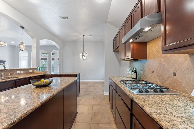 kitchen featuring visible vents, light stone countertops, under cabinet range hood, stainless steel gas cooktop, and a sink