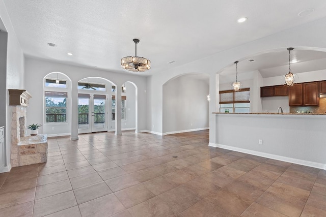 unfurnished living room with arched walkways, light tile patterned floors, recessed lighting, a textured ceiling, and baseboards