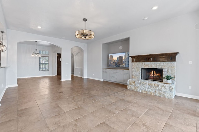 unfurnished living room featuring arched walkways, recessed lighting, an inviting chandelier, a stone fireplace, and baseboards