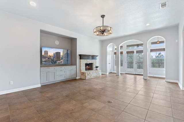 unfurnished living room featuring french doors, a stone fireplace, visible vents, arched walkways, and baseboards